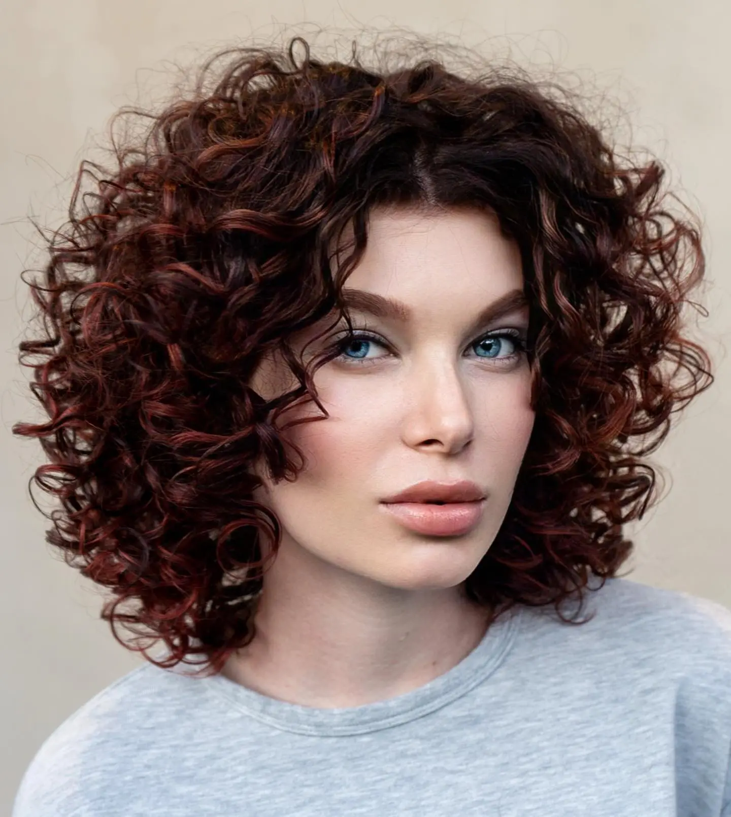 Femme avec un bob bouclé volumineux en forme de S, coupe courte et dégradée mettant en valeur les traits du visage avec des boucles bien définies.