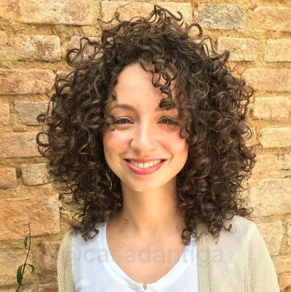 Femme avec cheveux bouclés mi-longs et coupe dégradée, volume équilibré et mèches encadrant le visage pour mettre en valeur les traits.