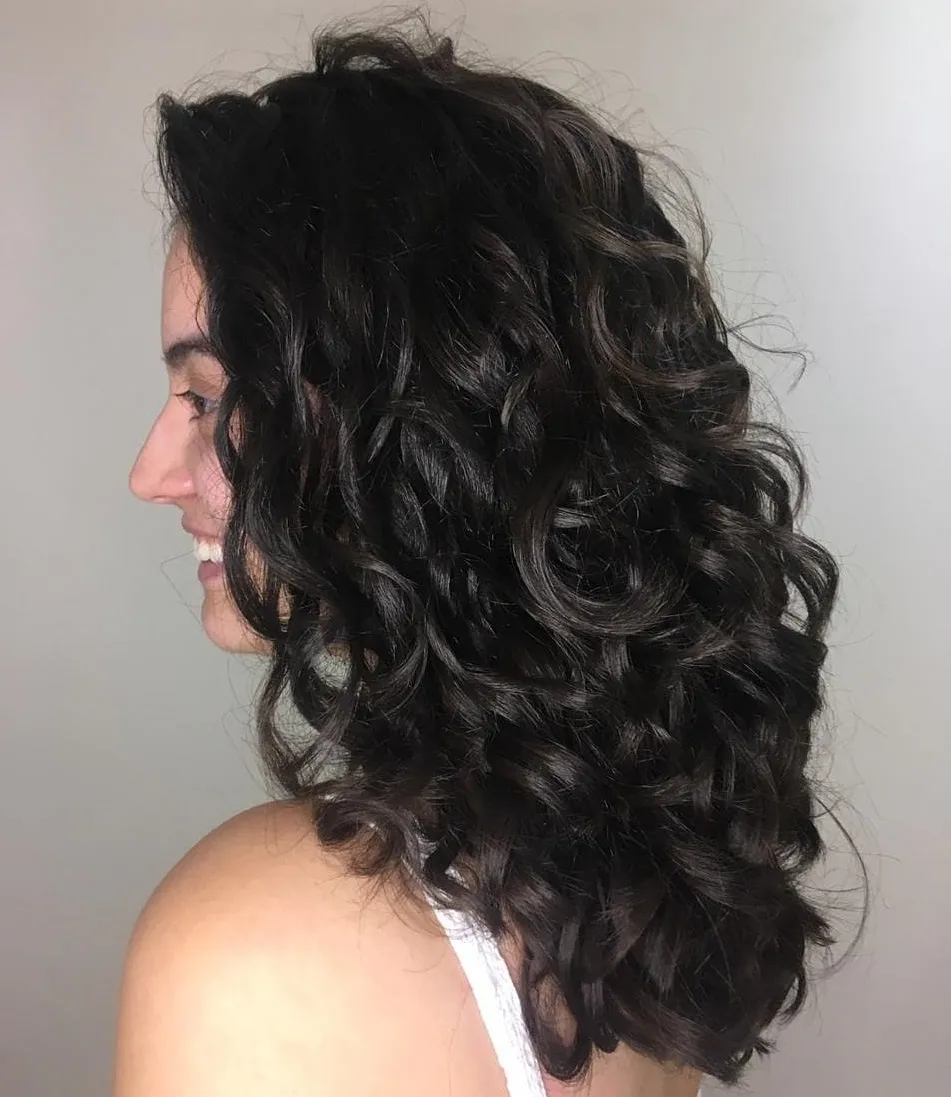 Femme avec une coupe longue en U sur cheveux ondulés, couleur brun foncé brillante et reflets naturels.