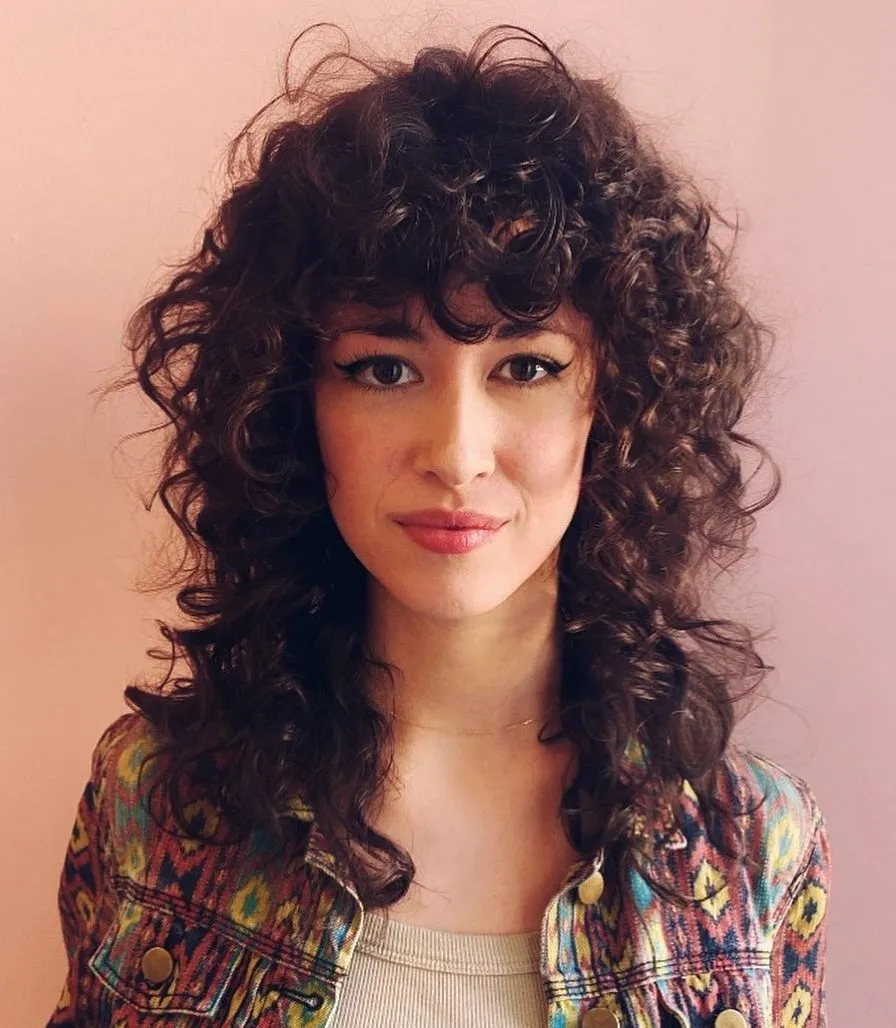 Femme avec une coupe shag mi-longue aux épaules, boucles volumineuses mises en valeur par des couches texturées et un dégradé dynamique.