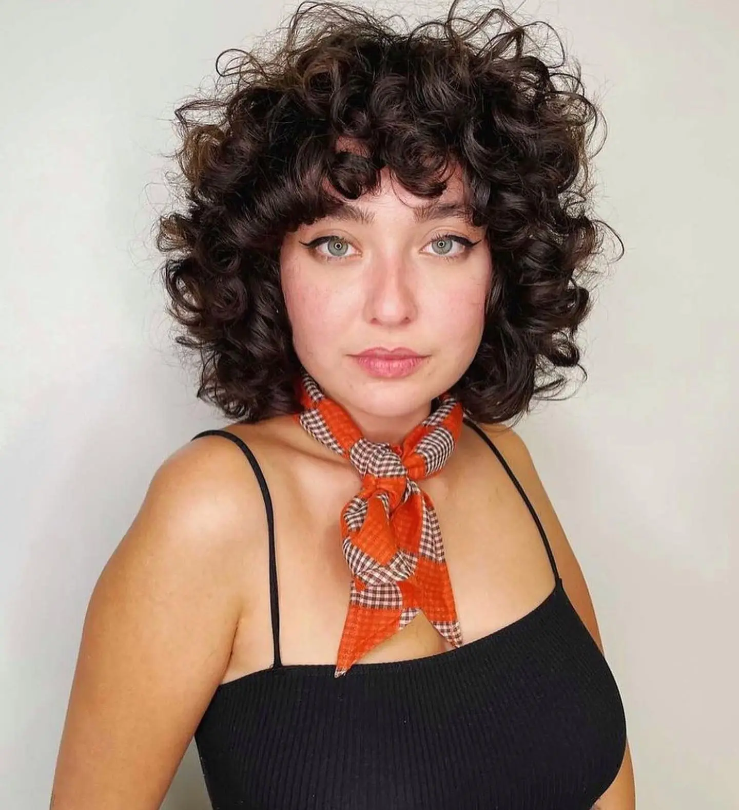 Femme avec un dégradé bouclé épais au-dessus des épaules, frange courte et volume allégé pour un look structuré et naturel.