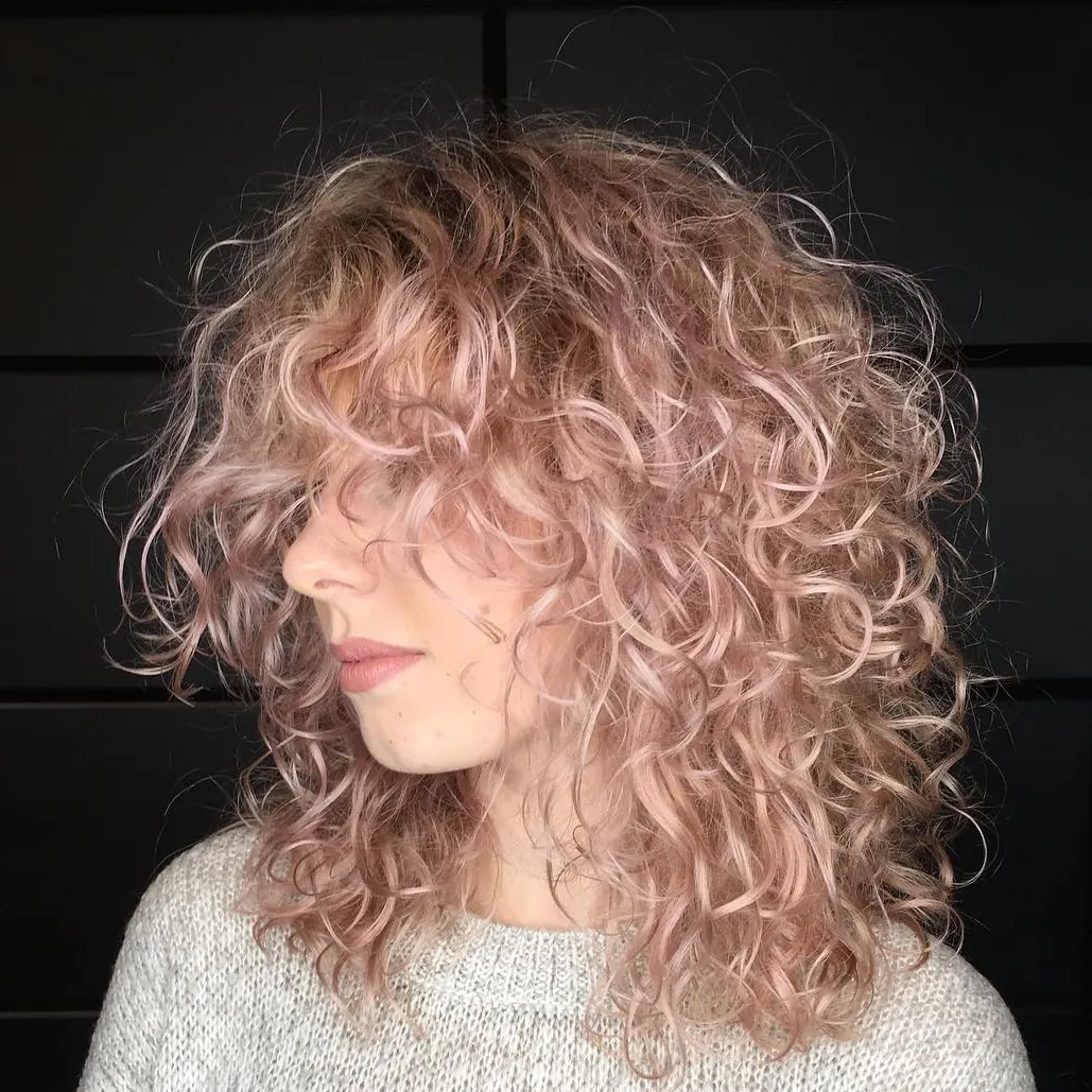 Femme avec des mèches roses-blondes sur cheveux ondulés, coloration tendance apportant une touche douce et féminine au look.