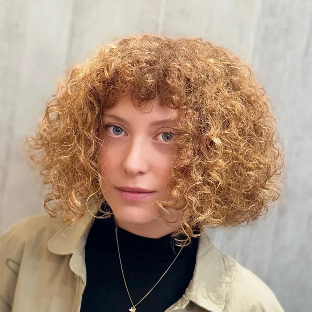 Femme avec un bob bouclé accompagné d’une frange, coiffure moderne qui encadre le visage avec souplesse.