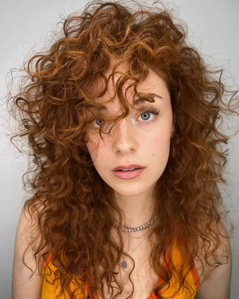 Femme avec une coupe longue dégradée pour cheveux bouclés, mise en valeur des boucles avec contraste subtil entre les longueurs.