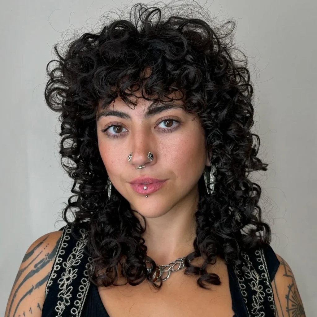 Femme avec une coupe wolf bouclée longue et frange, mélange de volume naturel et de style décontracté.