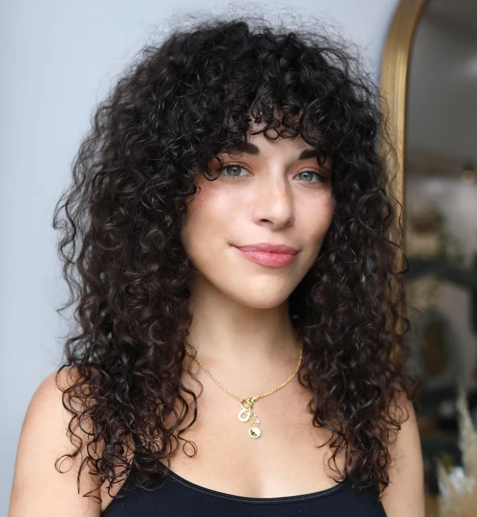 Femme avec une frange pour cheveux bouclés, coupe moderne qui souligne les traits du visage et la texture naturelle.