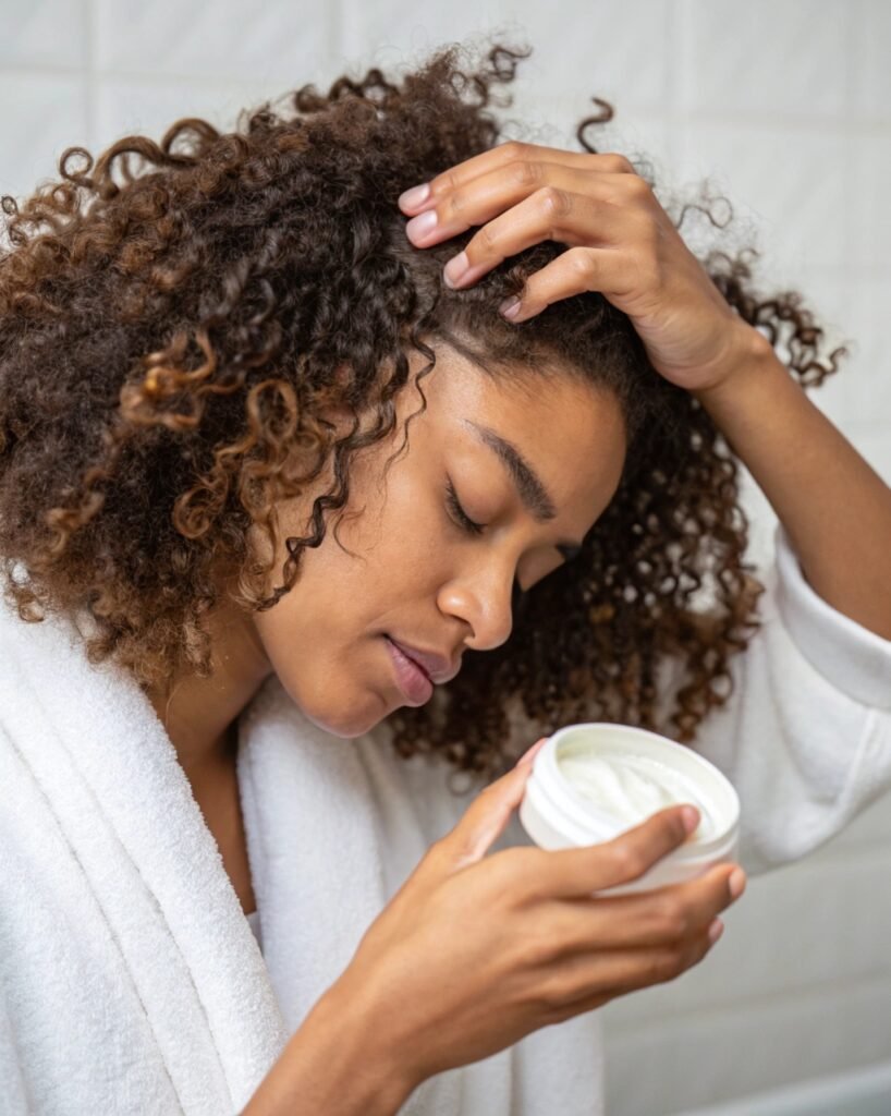 Application de Produits pour Cheveux Bouclés - Soins Capillaires en 2025 Personne appliquant un produit capillaire nourrissant sur ses cheveux bouclés, illustrant l'importance des soins adaptés pour des boucles saines et définies.