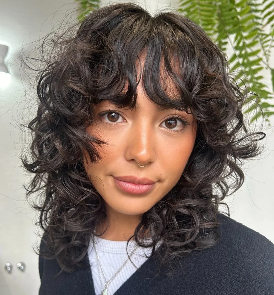 Femme avec un shag bouclé mi-long, coiffure légère et structurée idéale pour maîtriser les boucles volumineuses.
